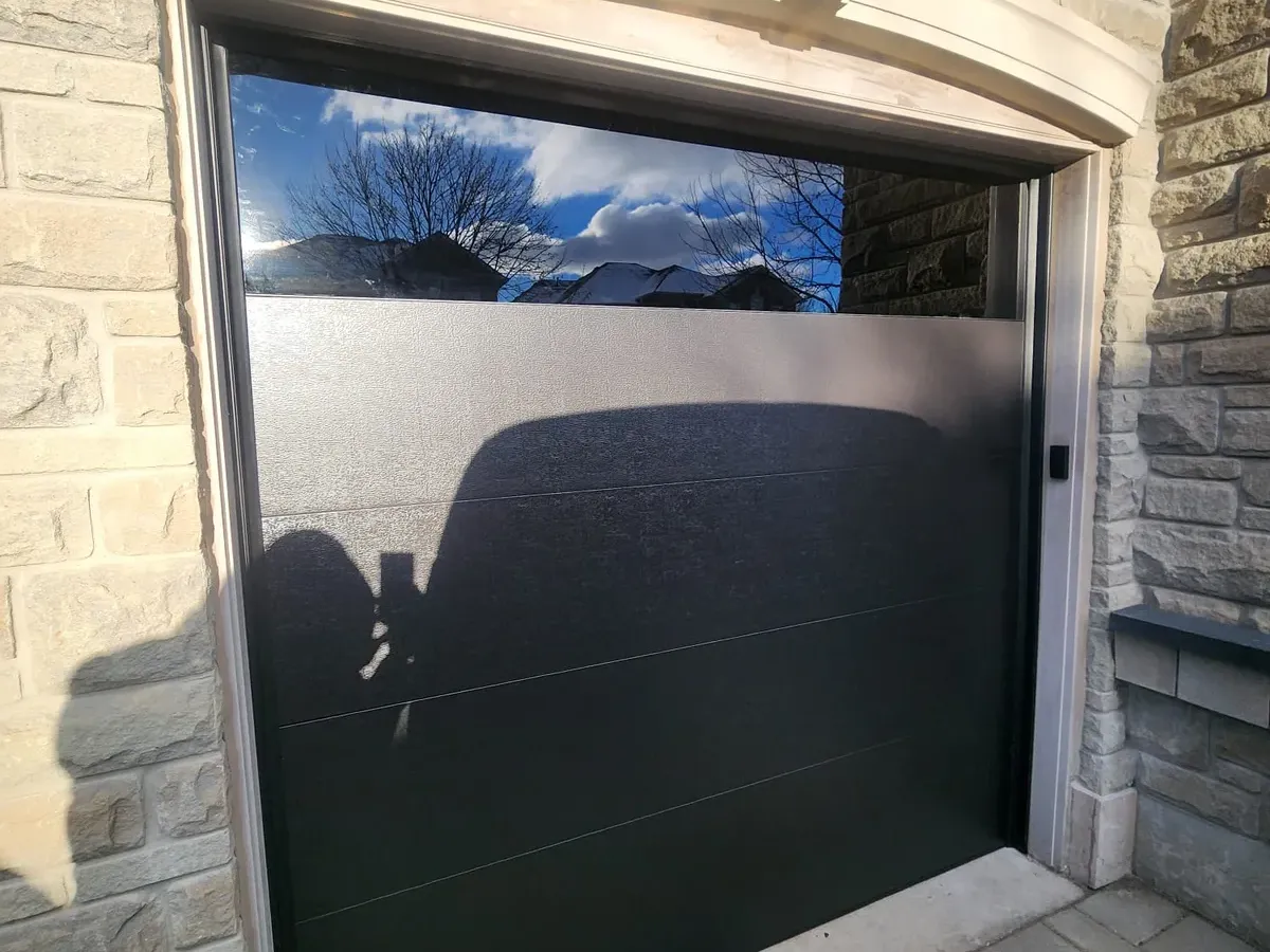 Black modern single garage door with glass strip on stone home — Toronto