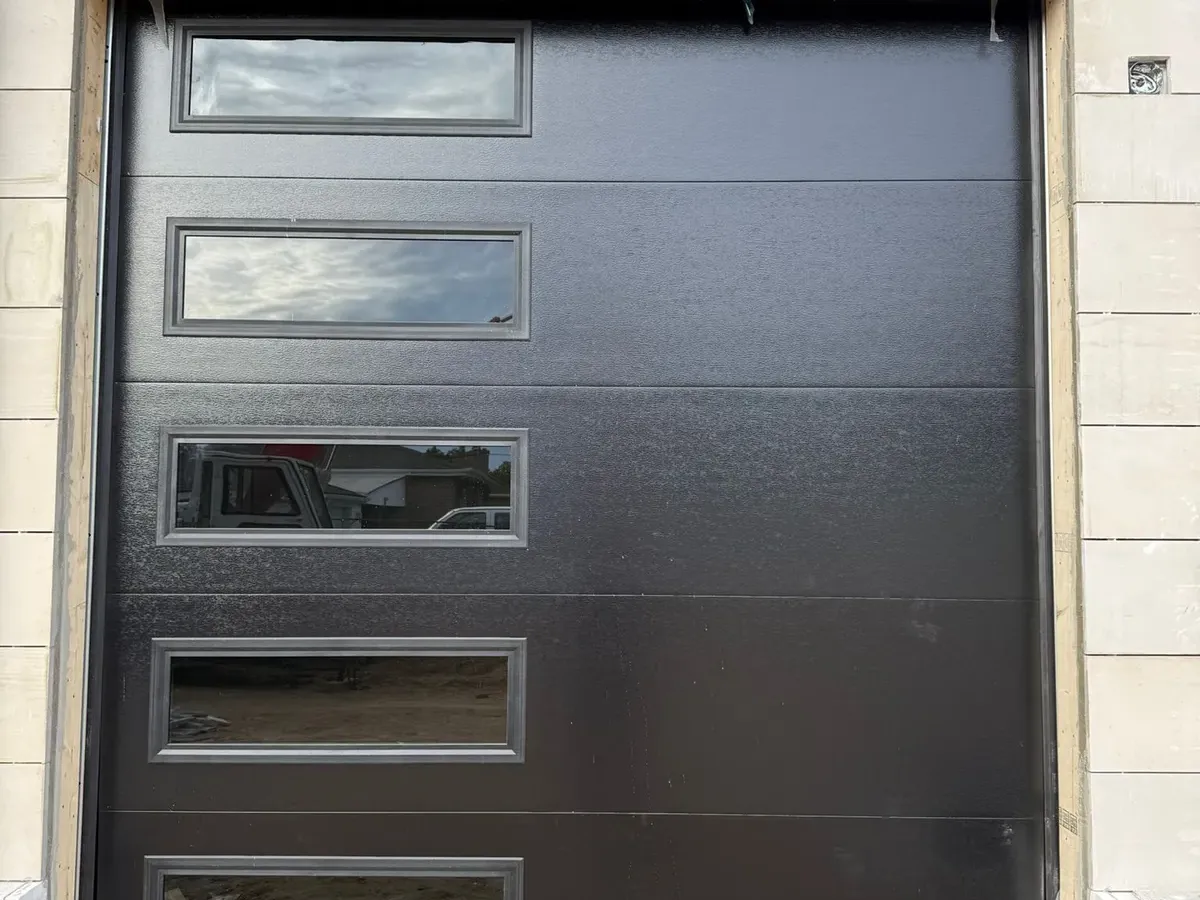 Dark charcoal modern flush-panel garage door with glass on stone home
